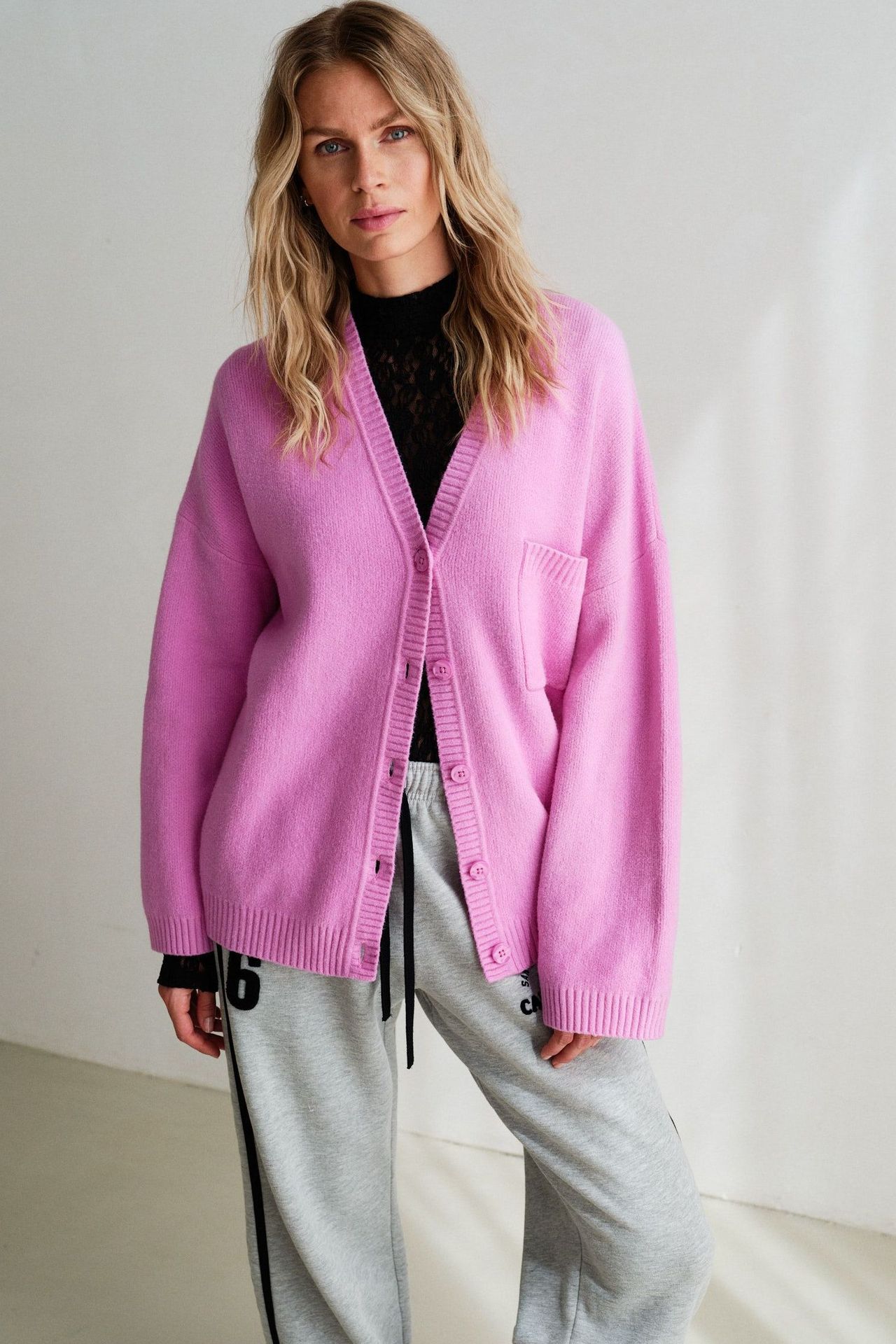 Frau trägt pinken Cardigan über schwarzem Top mit grauen Jogginghosen, lässiger Look.