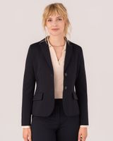 Frau im dunklen Blazer mit beige Bluse und Hose, professionell gekleidet, lächelnd.