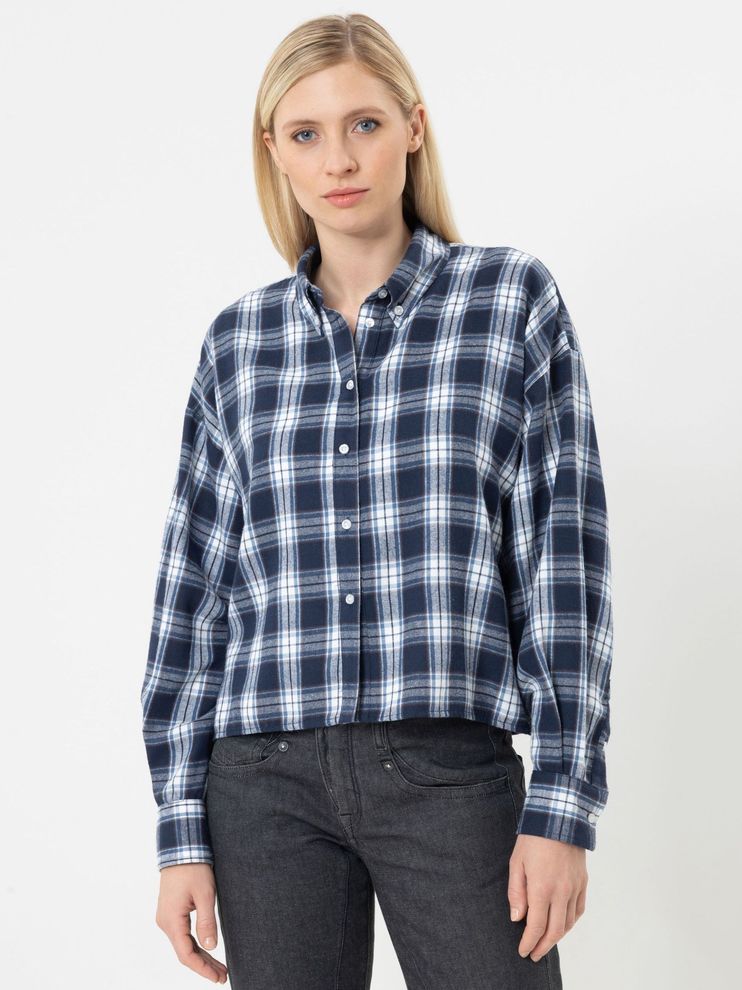 Frau trägt oversized kariertes Hemd mit dunkelblauen und hellen Streifen, schwarze Jeans.
