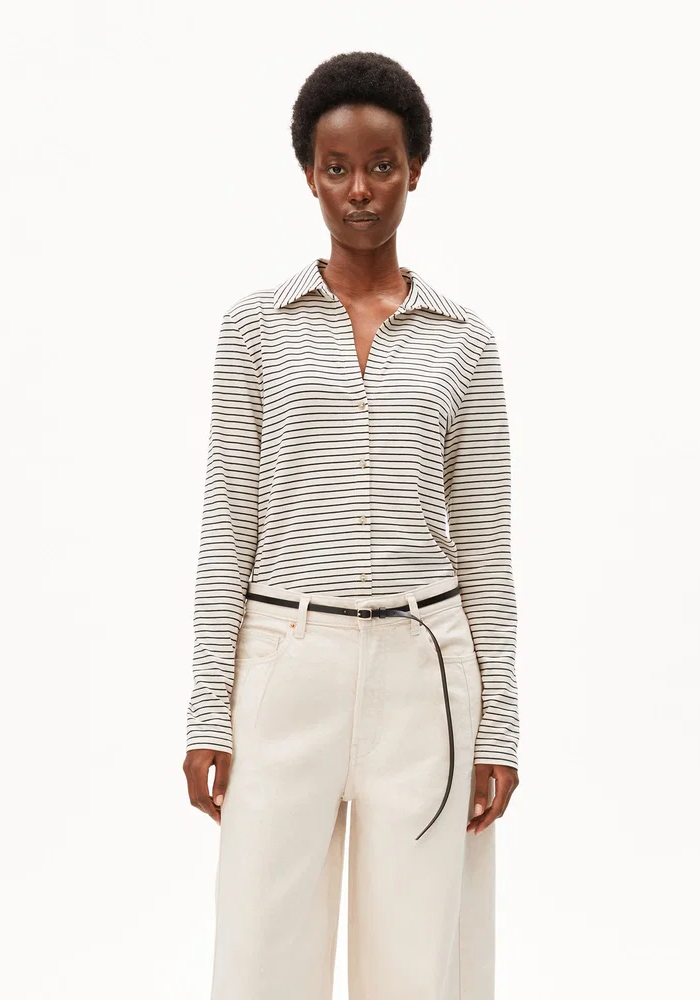 Frau trägt hellbeige, weite Hosen mit gestreiftem Langarm-Shirt und flachen Schuhen, schlichter Look.