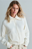 Frau trägt cremefarbene Cropped-Jacke mit Zipfel und beige weite Hose, lässig posierend.