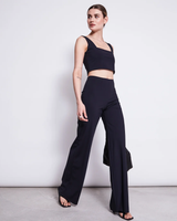 Frau trägt schlichtes schwarzes Crop-Top mit weiten, hochgeschlitzten Hosen, elegant posierend.